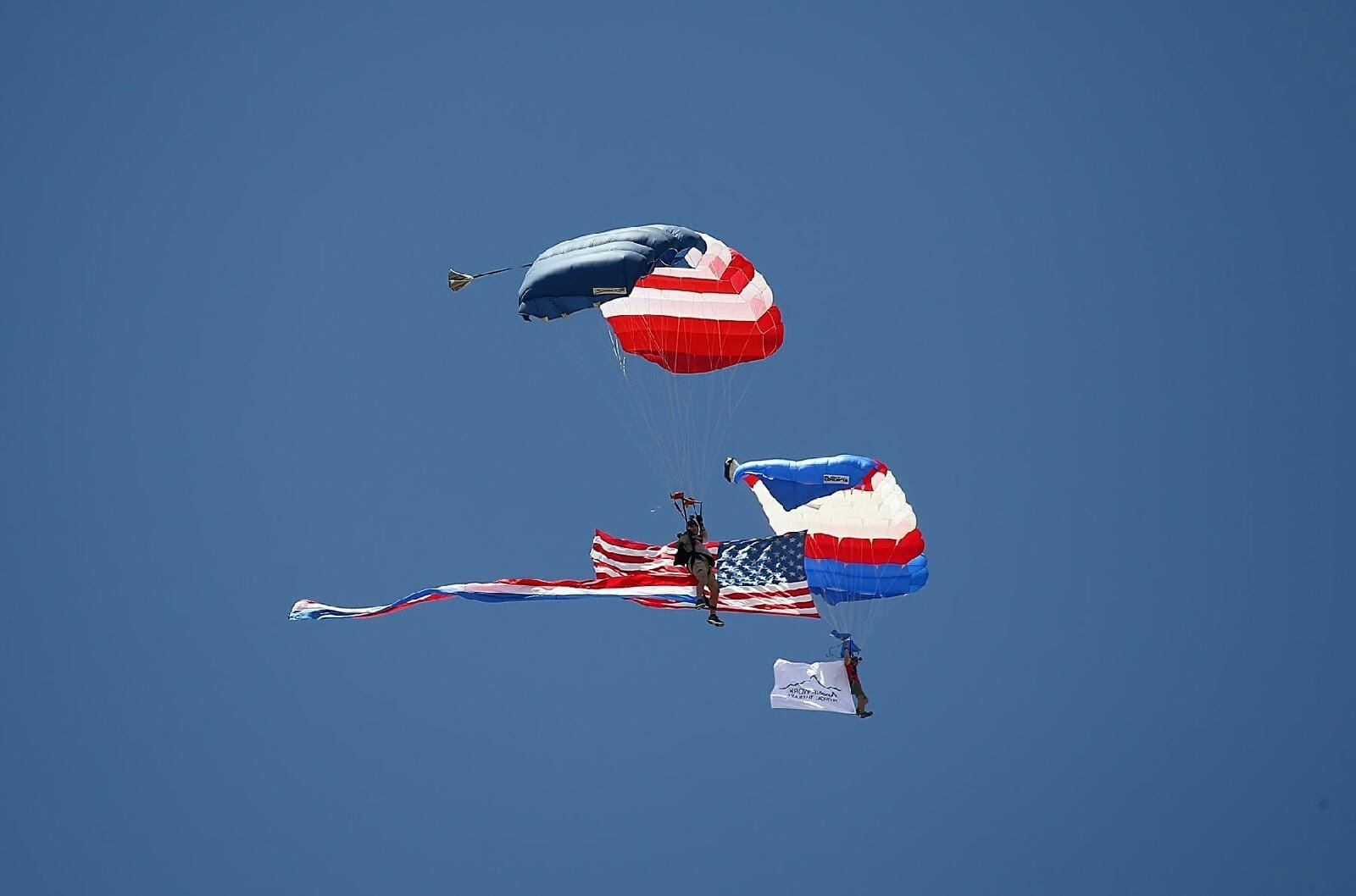 Two parachutes are flying in the sky with flags.