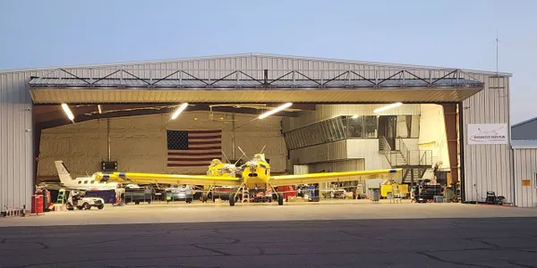 A yellow airplane parked in front of an airport hangar.