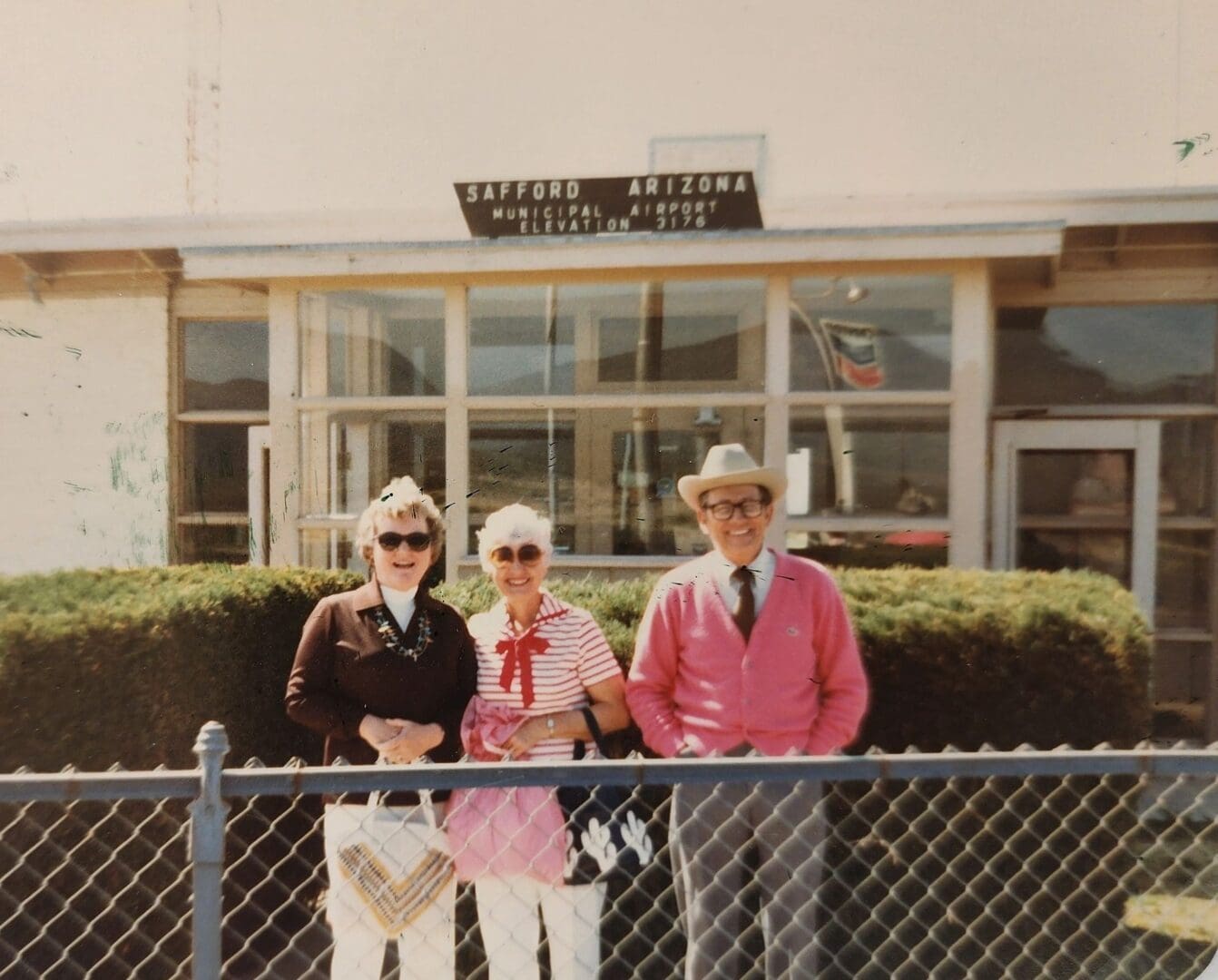 Three people standing in front of a fence.