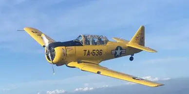 A yellow airplane flying in the sky with clouds