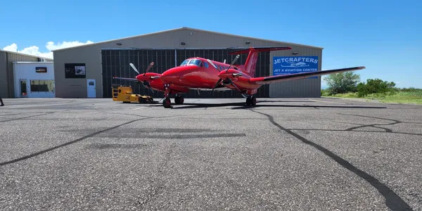 A red airplane parked in front of an airport hangar.